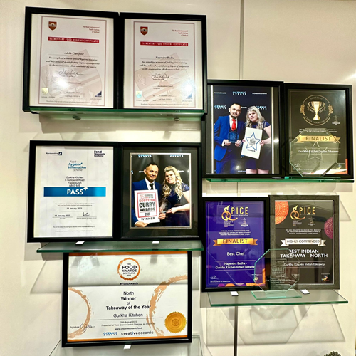 A wall display of framed certificates, awards, and photos of a restaurant and its staff.